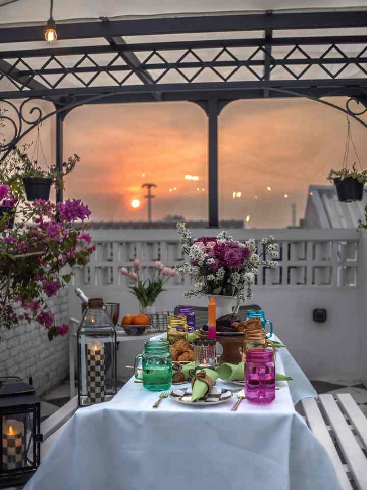 Balcony space with warm sunset hues and white walls, featuring a table set with vases and candles creating a cozy home party atmosphere