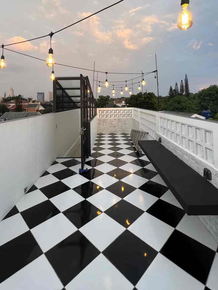 Modern terrace space with black and white checkerboard floor and string lights, featuring an outdoor bench with ambient setting