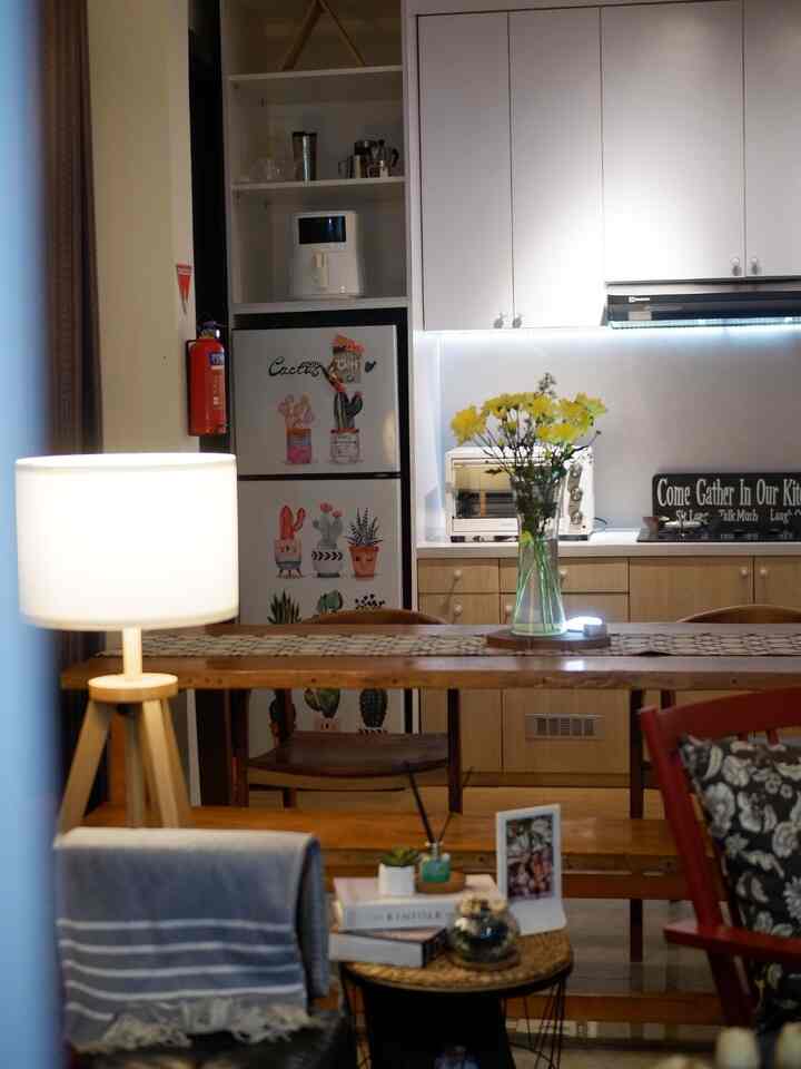 A cozy living and dining space featuring white and wood tones with kitchen cabinetry, a floor lamp, and a vase of yellow flowers on the dining table