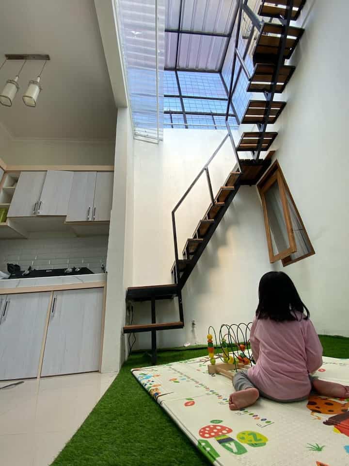 Natural color tone studio apartment featuring a kids play area with synthetic grass carpet and compact kitchen with open staircase
