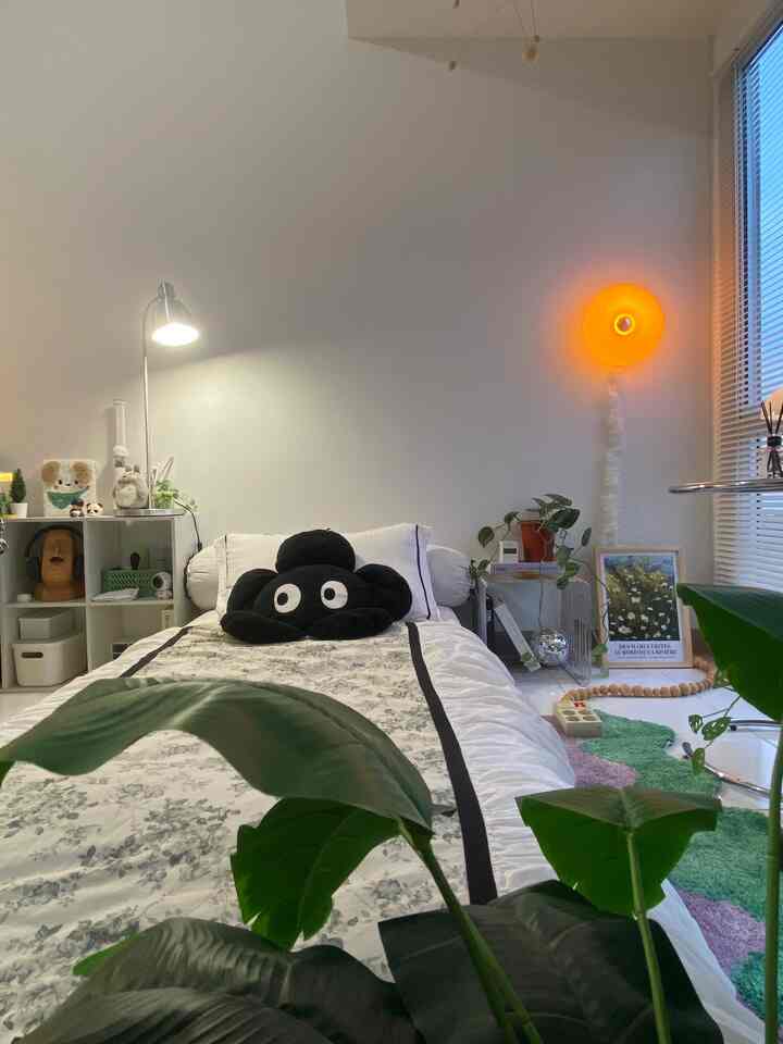 Natural color and white-toned small single bedroom featuring bed, floor lamp, and plants with cozy atmosphere