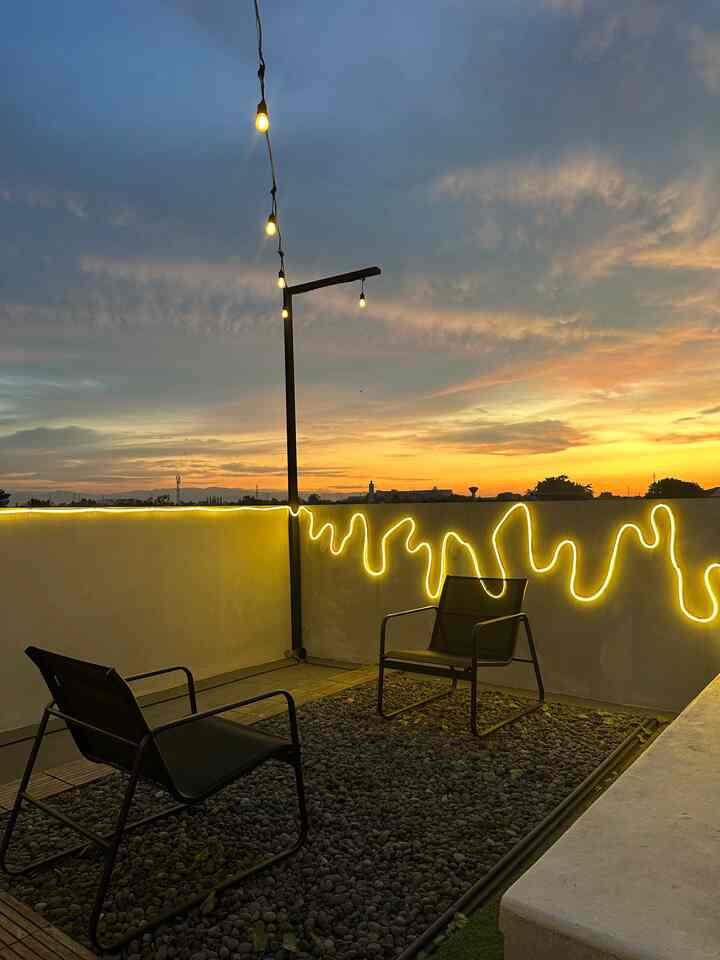 Gold-toned lighting with black outdoor chairs on a balcony space, complemented by a sunset sky creating a warm atmosphere