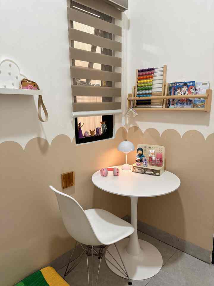 Beige and white toned kids' room with a small round desk and chair, wall shelf holding toys and books in a cozy setting
