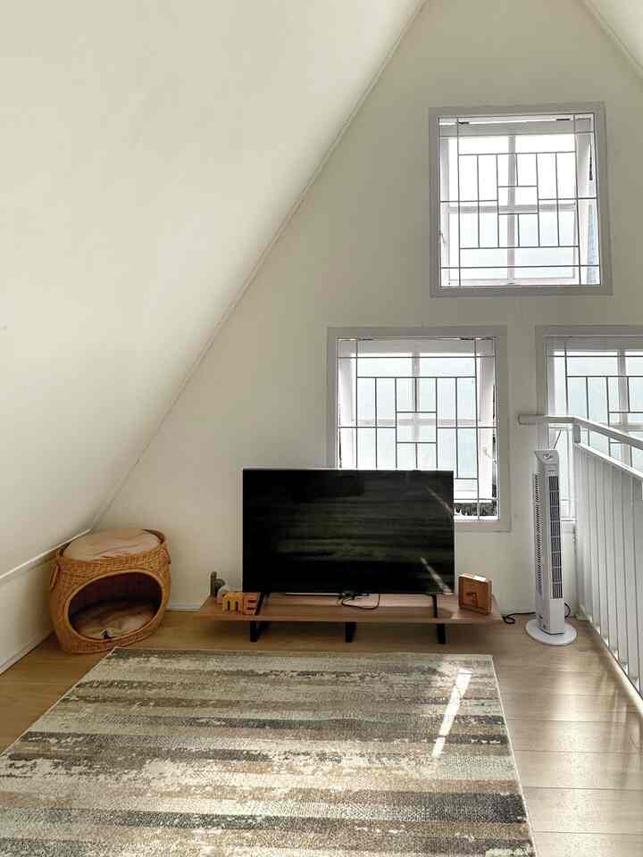 Natural wood tone flooring and white walls define a small living room with a pet bed and TV stand creating a cozy atmosphere