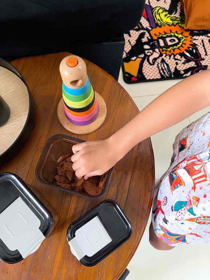 Brown wood round table in part of kitchen space with children's toys and storage containers on top