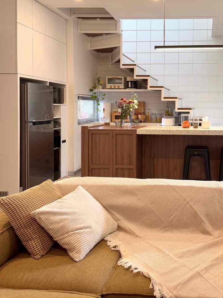 Natural-toned living room and kitchen space featuring beige sofa and wooden kitchen island with warm interior atmosphere