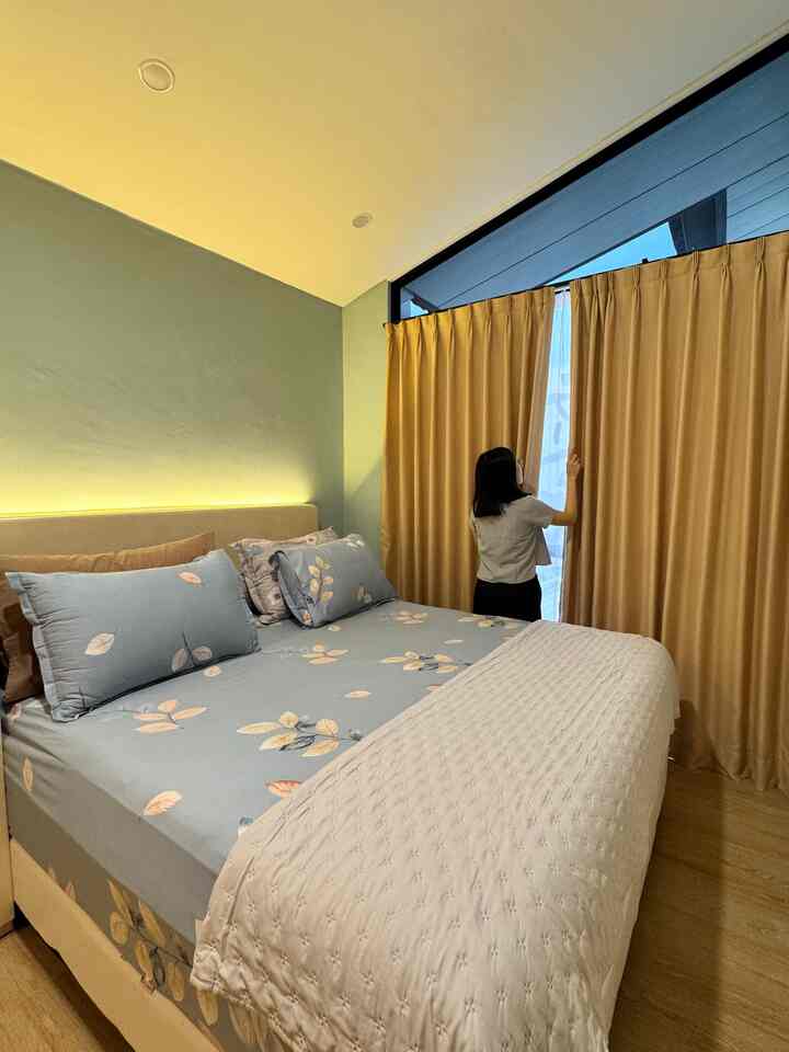 A cozy 6-tatami bedroom in soft green and white tones, featuring a large bed with quilted white bedding and leaf-patterned sheets, beside beige curtains.