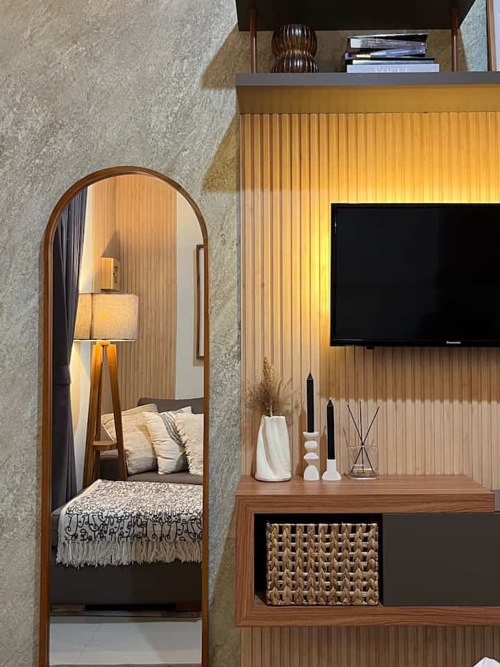 Warm-toned living room featuring wood tones and beige hues, with an arch mirror and TV creating a cozy atmosphere