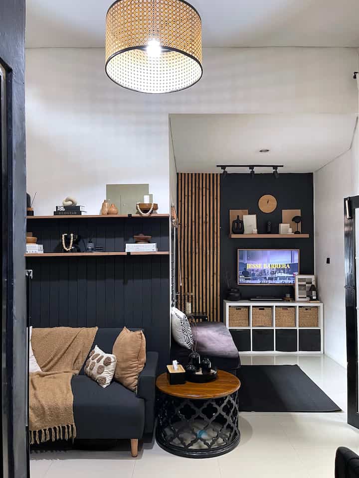 Compact living room with black and brown wood tones, featuring two sofas, a round coffee table, wall shelves, and a TV creating a cozy atmosphere