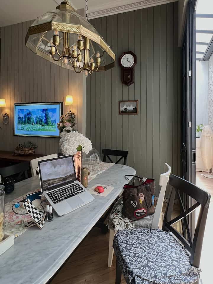 Dining room with natural color walls and wood tone floor, featuring a marble dining table, multiple chairs, vintage style lighting and clock