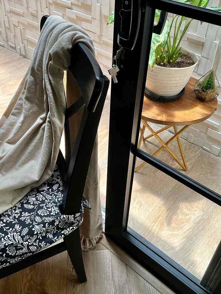 Cozy balcony entrance featuring warm wood tone flooring and black chair, decorated with plants and a round wooden side table