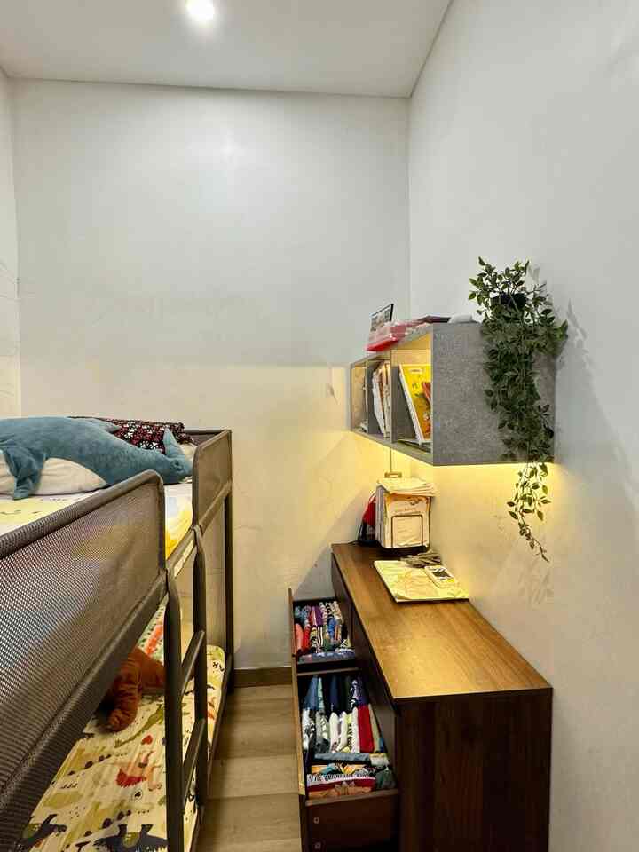 Kamar anak dengan desain minimalis ini dirancang untuk dua anak dengan fokus pada kenyamanan dan keamanan. Berikut deskripsinya:
1.	Bunk Bed Baja Minimalis
	•	Menggunakan bunk bed berbahan baja yang kokoh dan tahan lama.
	•	Dilengkapi dengan pinggiran pelindung di setiap sisi untuk mencegah anak terjatuh.
	•	Tinggi bunk bed dirancang tidak terlalu tinggi agar anak-anak mudah naik ke tempat tidur tingkat atas tanpa risiko.

2.	Dinding dengan Cat Easy Clean Dulux
	•	Dinding kamar dicat dengan Easy Clean Dulux, memungkinkan noda atau coretan dari anak mudah dihapus tanpa meninggalkan bekas.
	•	Warna cat tetap netral seperti putih atau krem agar memberikan kesan luas dan bersih.

3.	Rak Serbaguna
	•	Rak multifungsi untuk menyimpan baju seragam, tas sekolah, dan mainan anak.
	•	Penempatan rak dirancang agar mudah dijangkau oleh anak-anak.

4.	Penyimpanan Pakaian Harian
	•	Baju rumah disimpan di storage khusus yang terorganisir, seperti kotak penyimpanan atau lemari kecil, memudahkan anak mengambil sendiri pakaian mereka.

5.	Kabinet Terbuka untuk Buku
	•	Kabinet terbuka digunakan untuk menyimpan buku bacaan dan buku sekolah.
	•	Desain kabinet memungkinkan akses mudah bagi anak-anak untuk mengambil dan menyimpan buku sendiri.

6.	Lantai SPC Berwarna Cream
	•	Lantai SPC dipilih karena tahan lama dan memiliki tekstur yang aman untuk anak-anak.
	•	Jika anak terjatuh, lantai ini memberikan permukaan yang tidak terlalu keras sehingga mengurangi risiko cedera.

Keseluruhan desain kamar memberikan suasana nyaman, aman, dan mendukung kemandirian anak dalam mengatur barang-barang mereka sendiri.  

#tempattiduranak #catputih #cateasyclean #catdulux #storageanak #rakbuku 
#RumahRamahAnak
 #MaterialRamahAnak
 #FurniturRamahAnak
