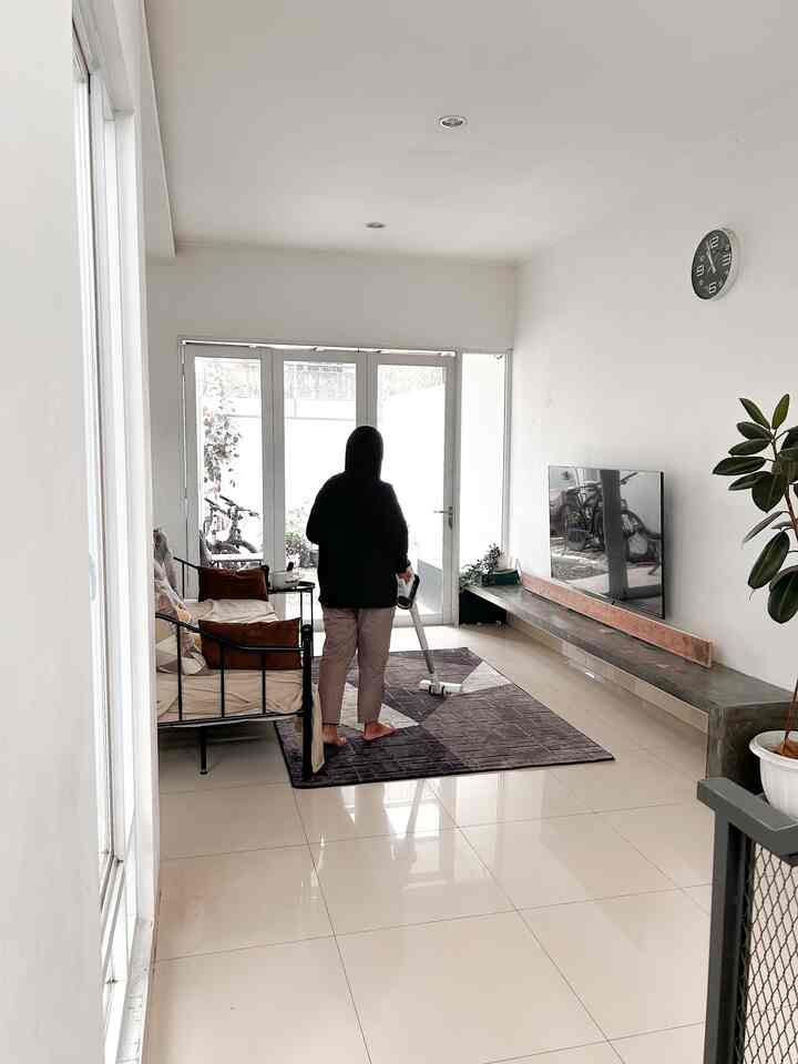 Bright ivory floor and white-walled living room featuring sofa on left, central carpet, TV with wall clock on right, in a simple Scandinavian style