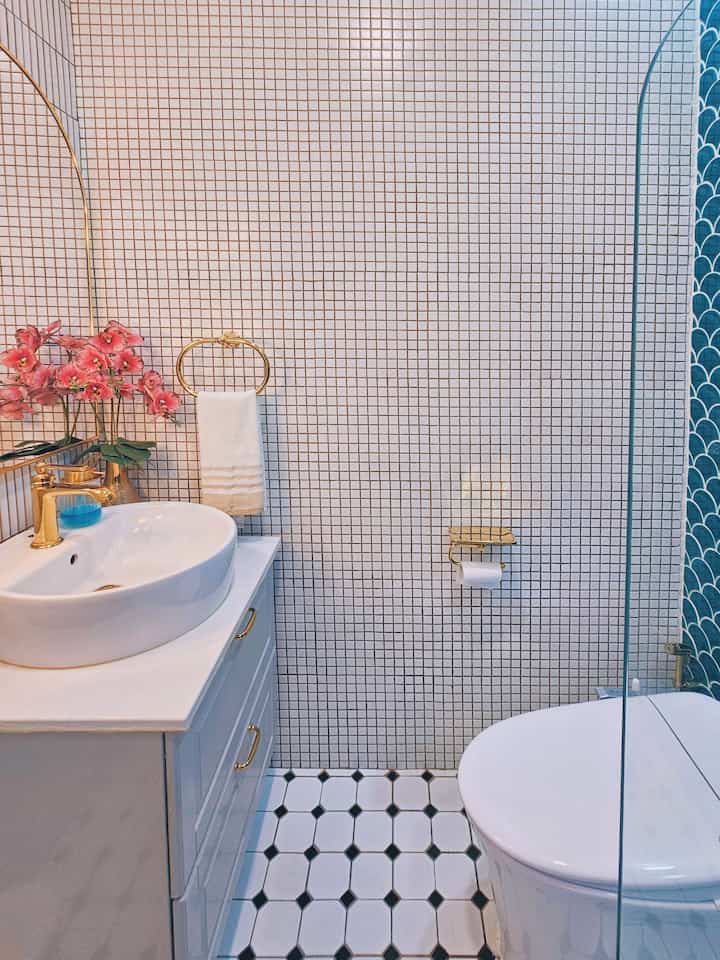 Modern restroom with white tiled walls and gold accessories, featuring a washbasin and toilet in a clean space