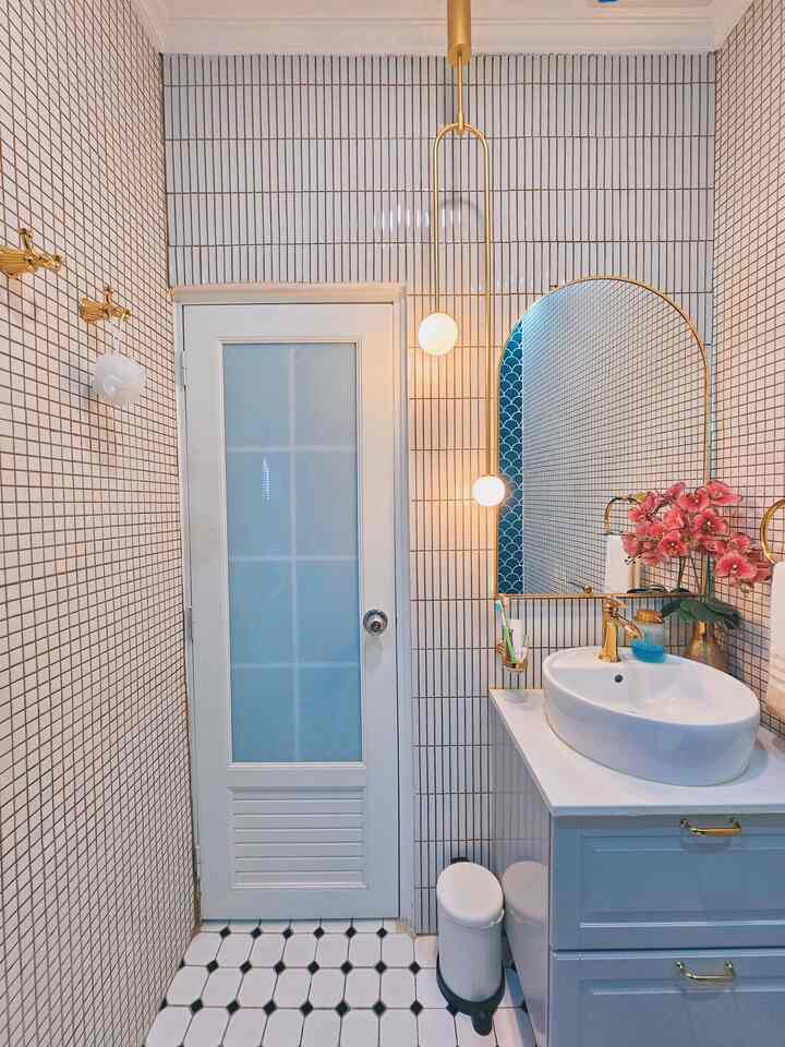 Bathroom with gold and white tones featuring an arched mirror and sink, creating a sleek atmosphere