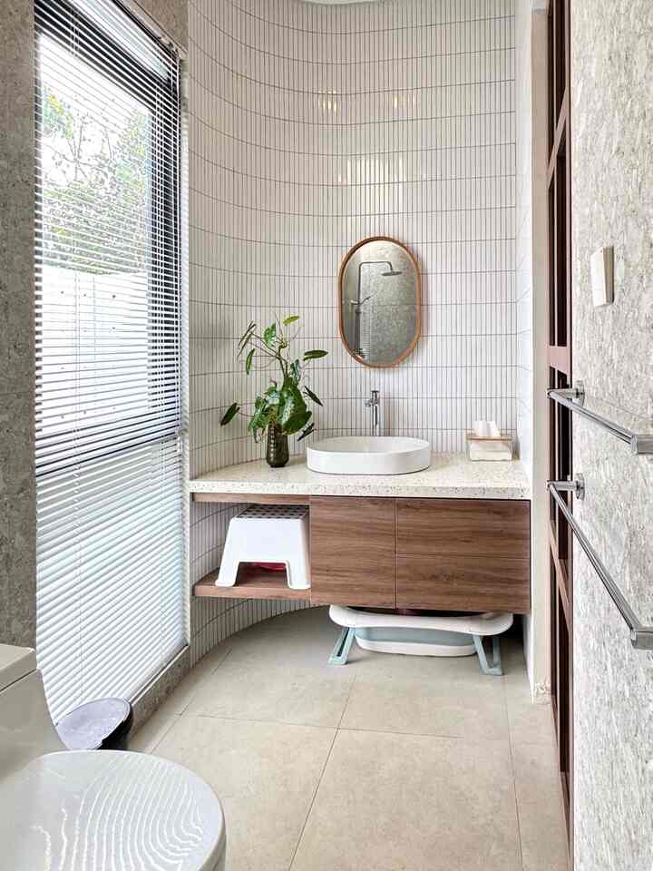 Bright bathroom featuring white tiles and wood-tone furniture with a plant, creating a warm and minimal atmosphere