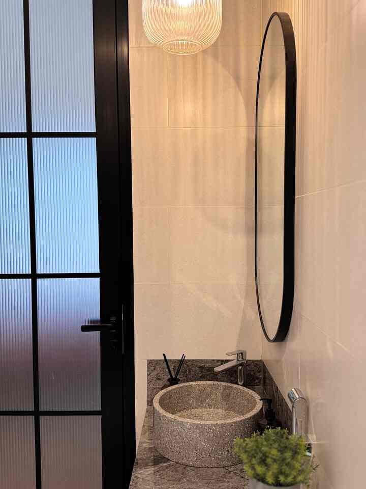 Modern natural-toned bathroom featuring a round mirror and stone sink with a sleek, elegant design
