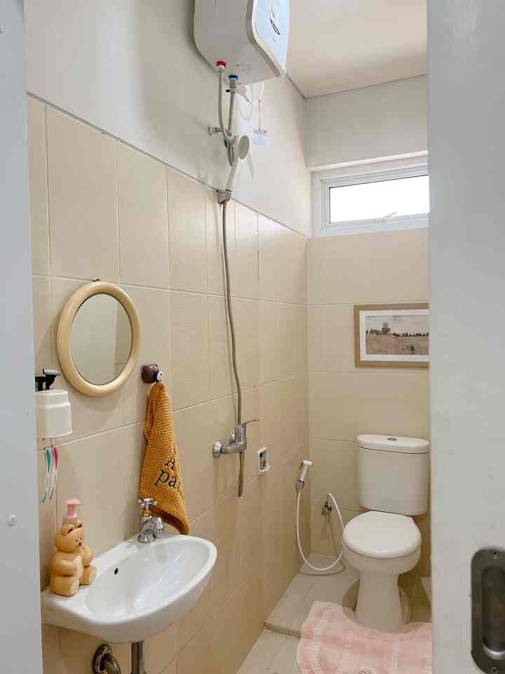 Natural-toned small bathroom featuring beige and white tiles, sink, toilet, and shower accessories with a cozy atmosphere