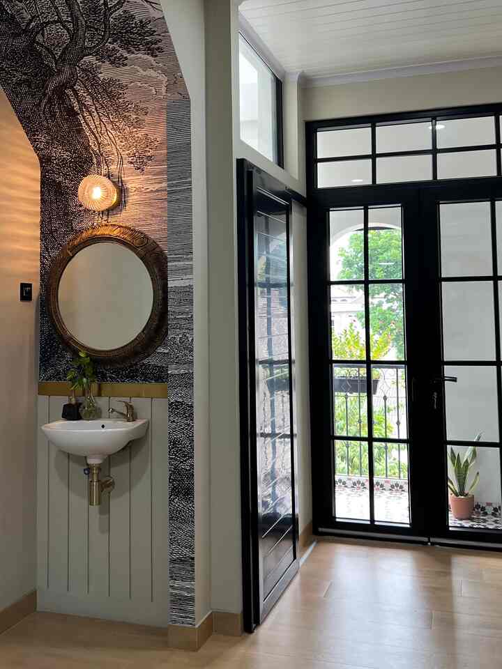 Natural-colored living and entrance space featuring black-framed glass doors, round mirror, and wall sconce in a clean modern design