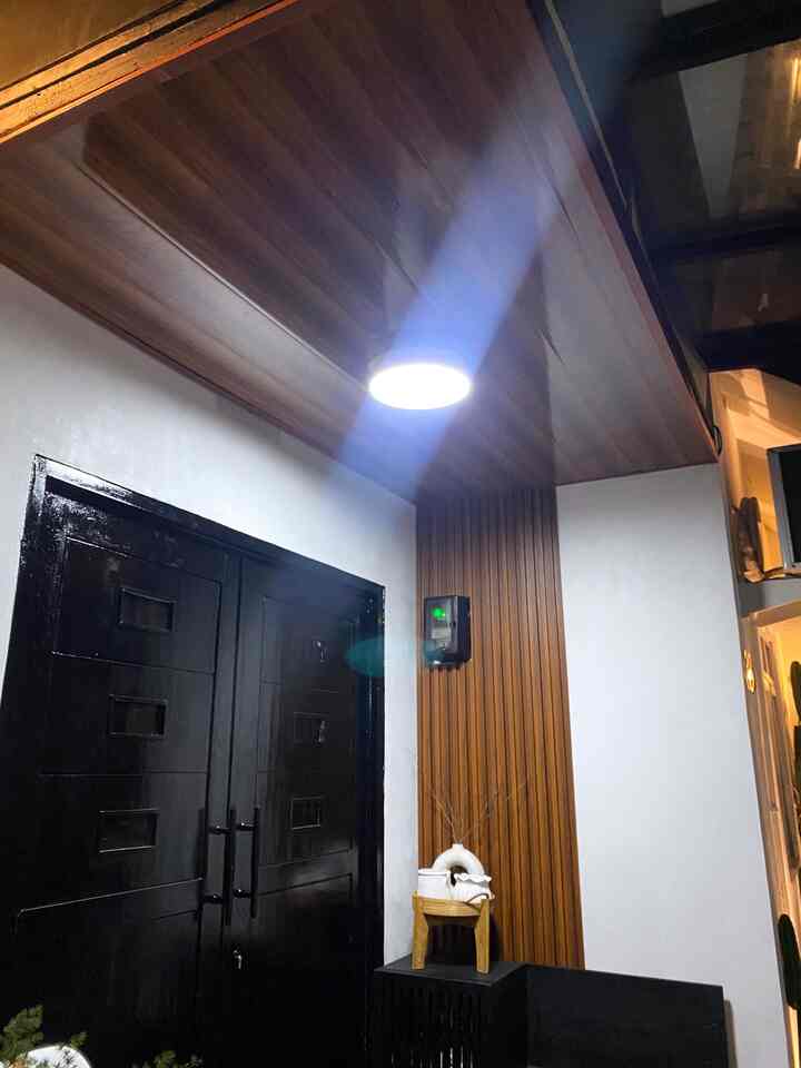 Modern entrance space with warm wood tone ceiling and wall panel, black double doors on left, and ceiling light illuminating area