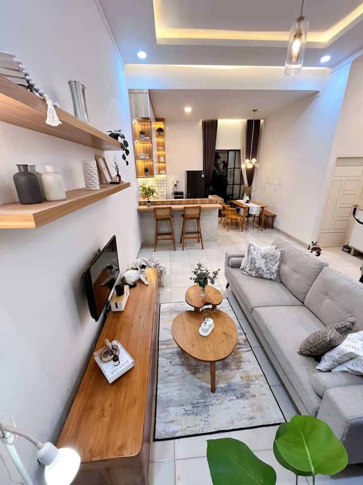 Natural-toned wood furniture and a gray sofa in an open living room with kitchen, cozy space featuring visible cats