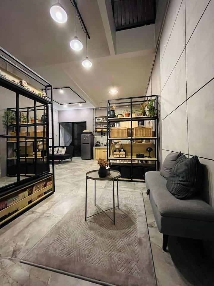 Modern natural tone open living room and kitchen featuring gray sofa and wood-tone open shelving with a cozy atmosphere