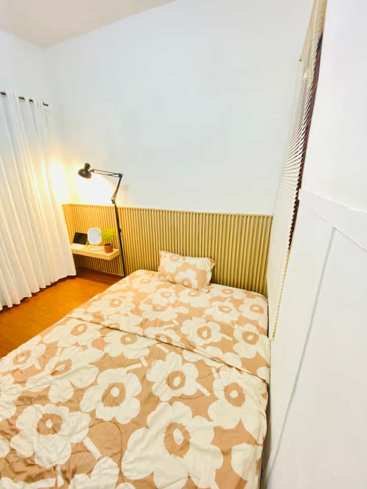 White and beige bedroom featuring floral bedding, nightstand, and floor lamp creating a simple and cozy atmosphere