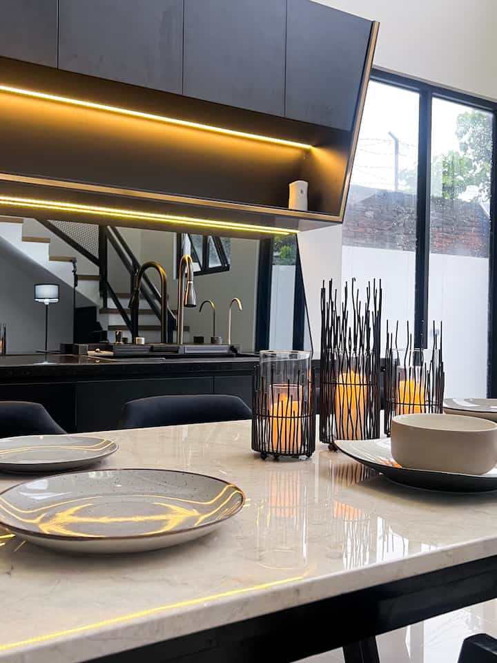 Modern kitchen in white and black tones featuring a large window, marble dining table, and warm LED mood lighting with a clean atmosphere