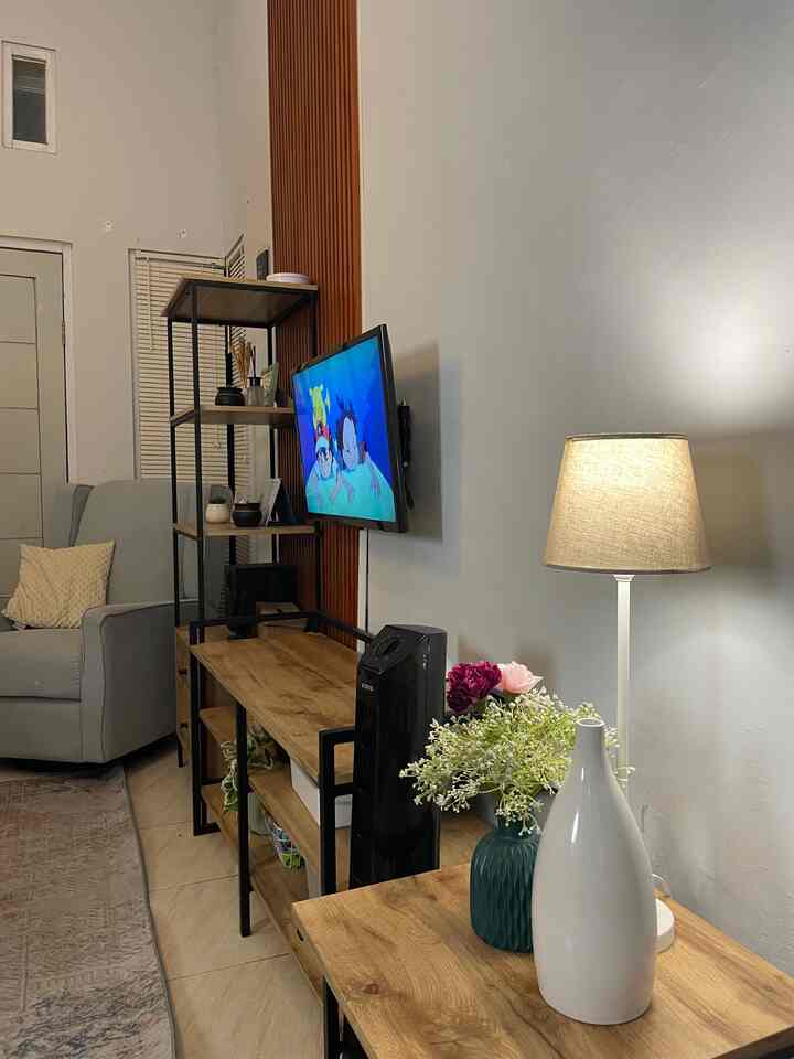 White and wood tone living room featuring sofa and wall-mounted TV with a simple natural ambiance
