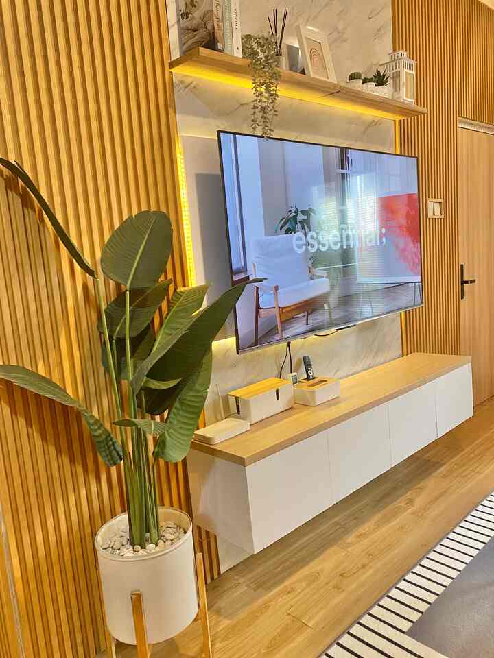 Warm and minimal living room with wood tone slatted walls, white TV cabinet, and large potted plant
