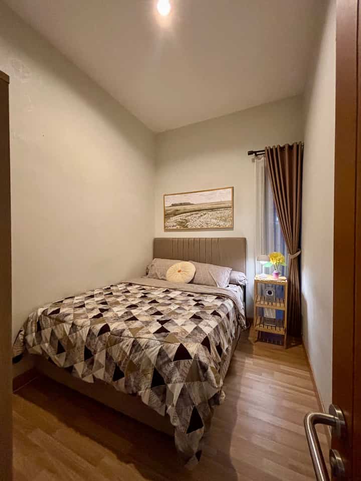 Warm wood tone compact bedroom featuring a bed and nightstand with table lamp creating a cozy atmosphere