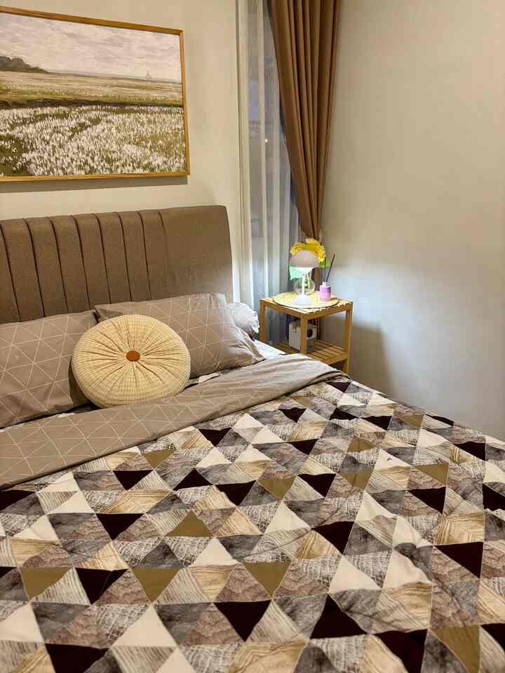 Beige and brown toned bedroom featuring a bed with round cushion and wall decor, creating a cozy atmosphere