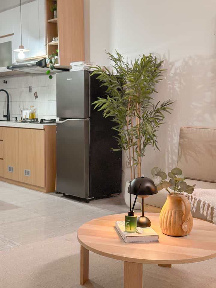 Natural-tone living room and kitchen space featuring a wooden coffee table, sofa, black refrigerator, and green plant with cozy atmosphere