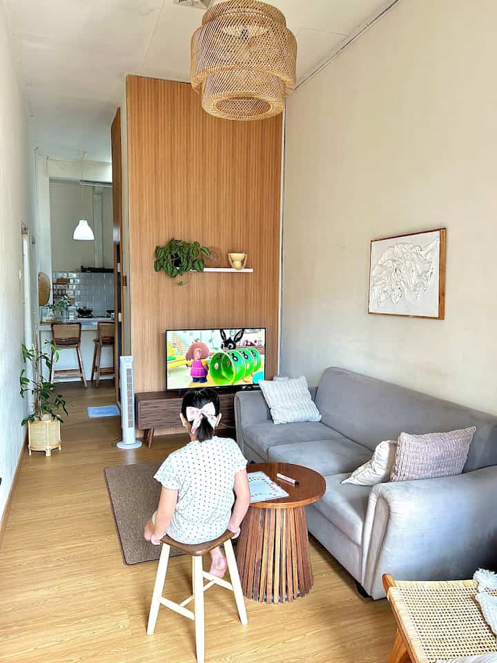 Warm wood-toned natural living room featuring gray sofa, wooden wall panel, carpet, and floor lamp creating cozy atmosphere