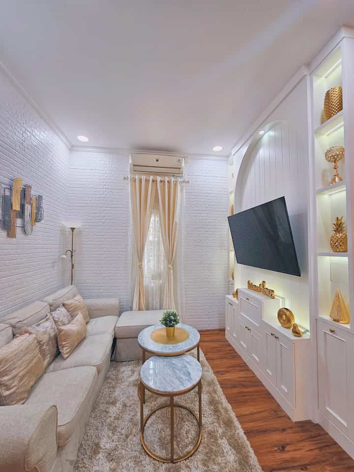 Natural modern living room with white walls, wood-tone flooring, gold accents, beige sofa, and curtains creating a cozy atmosphere