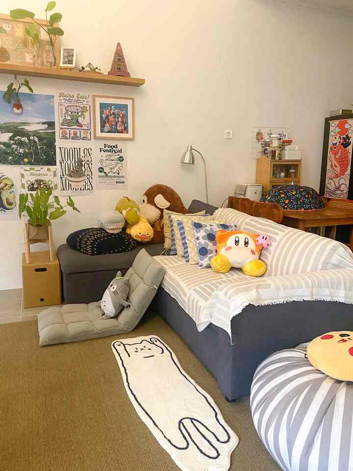 A cozy living room in soft beige and gray tones featuring a sofa with various cushions and plush toys, complemented by wall art decorations