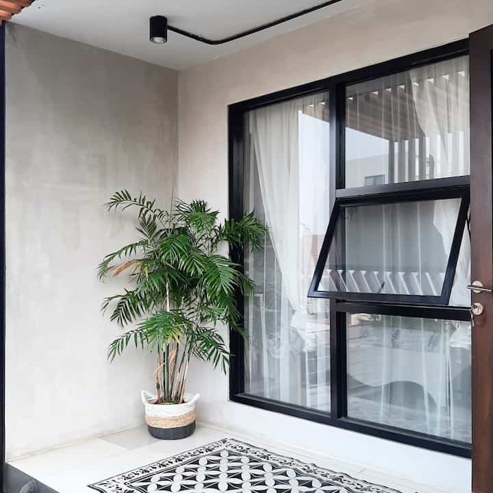 Modern veranda with gray walls and black window frames featuring a green palm plant and patterned floor tiles