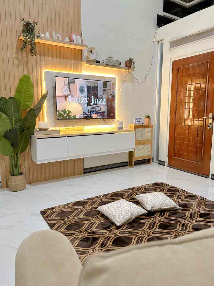 White and wood tone living room featuring TV with white floating TV stand, brown patterned rug and cushions creating a cozy space