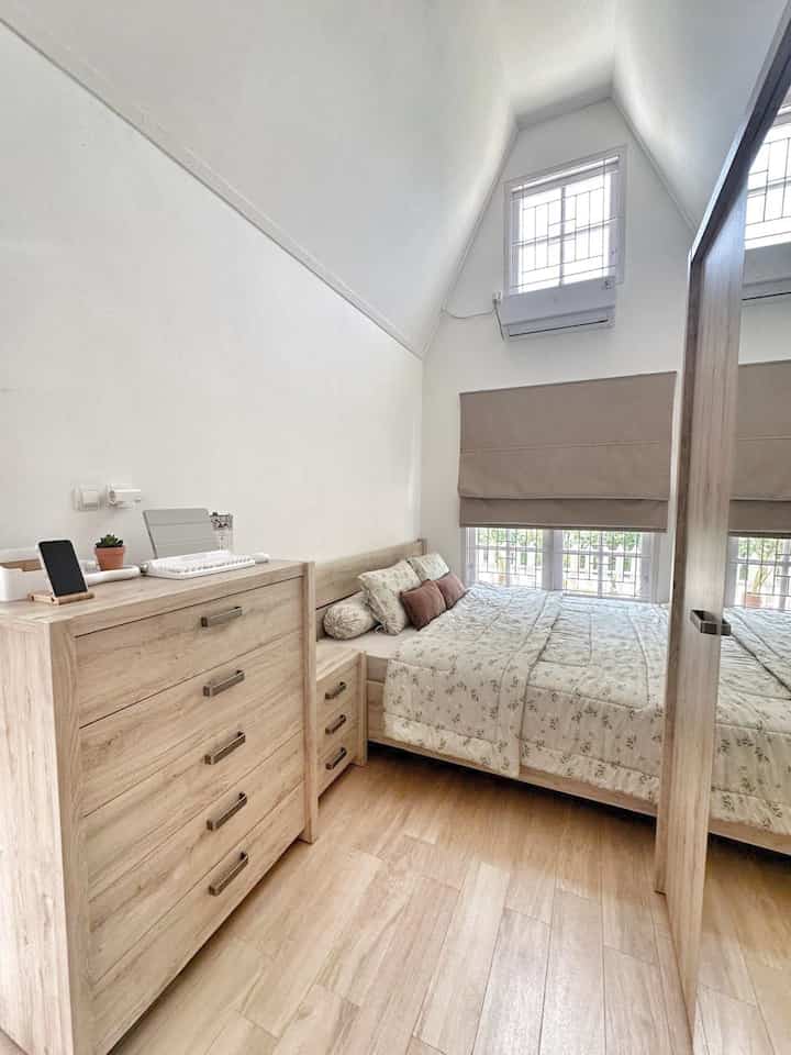 Compact bedroom featuring wood tone furniture and beige accents, with wardrobe and dresser creating a cozy space
