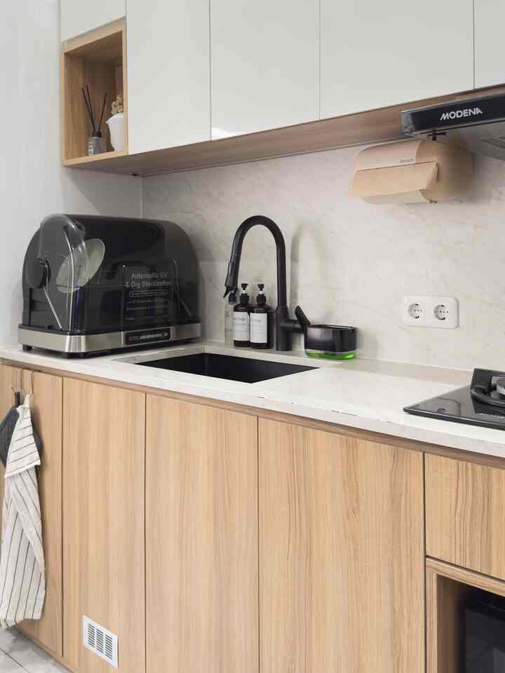 A clean kitchen with white and natural tones, featuring a black faucet and dish sterilizer on marble countertops