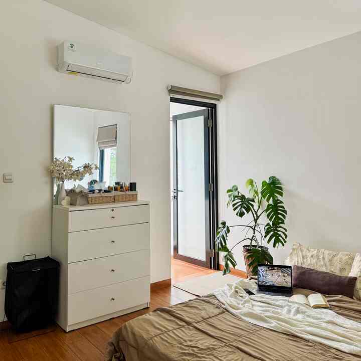 Natural 6-tatami sized bedroom with white walls, wood-tone floor, bedspread, dresser with mirror, and a green plant