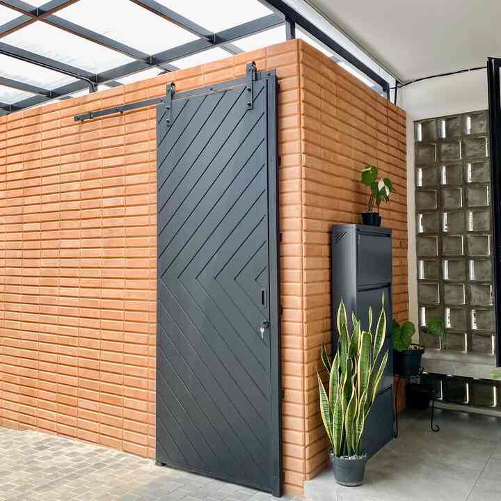 Light brown brick entrance area featuring a dark gray sliding barn door, potted plants and a storage cabinet with a clean aesthetic