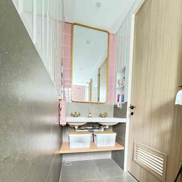 Bright bathroom featuring pink tiles and gold accents, large central mirror with sinks and storage baskets below, modern style