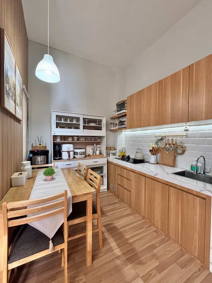 Natural wood tone and white walls define this small modern kitchen and dining area with warm pendant lighting