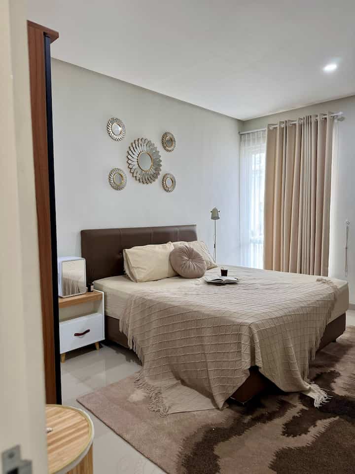 Beige-toned bedroom featuring bed with beige throw blanket and gold wall mirror decorations creating a warm atmosphere
