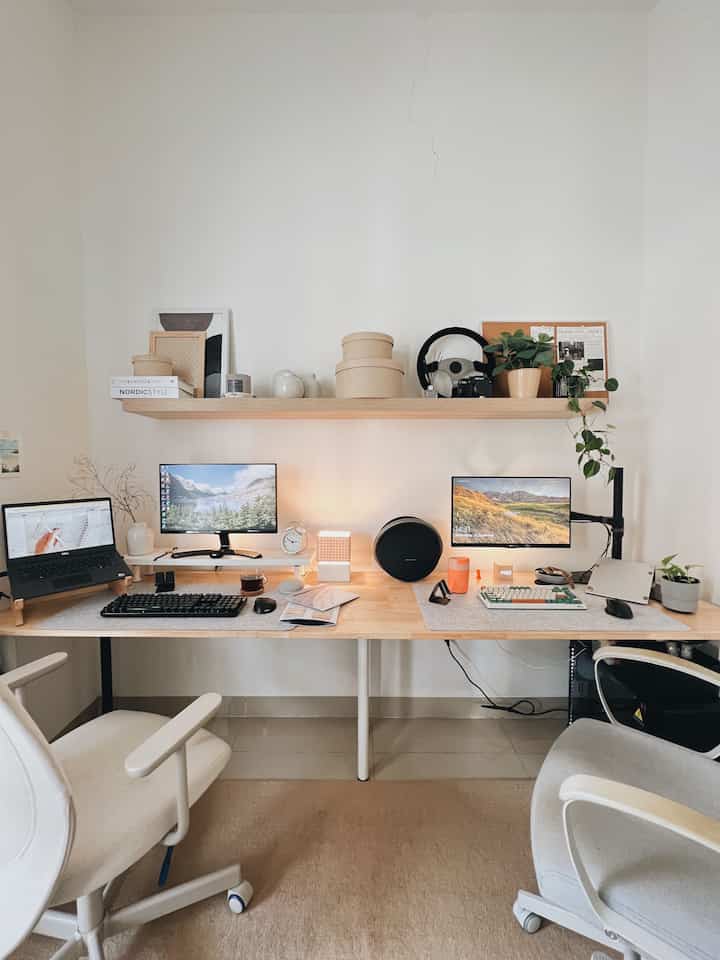 Modern home office with white walls and wood tone desk featuring dual monitors and office chairs in a neat workspace