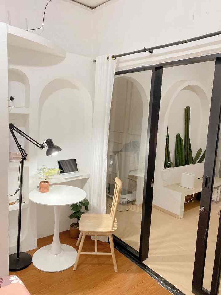 White-tone small home office space featuring round table, wooden chair, floor lamp, and cacti with natural and minimalist interior design
