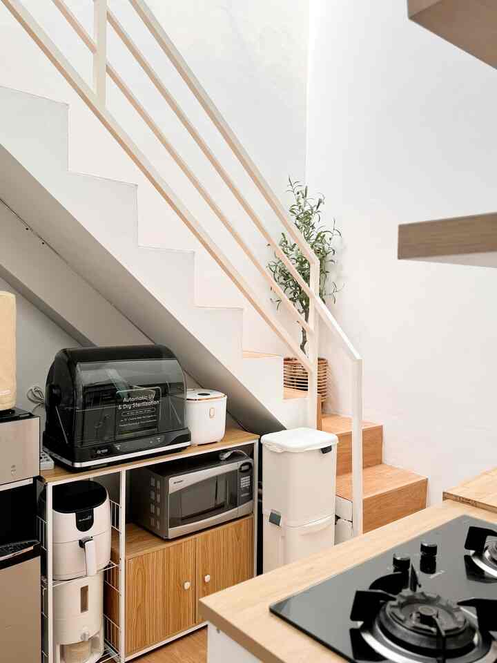 Bright kitchen space with white walls and natural wood-tone stairs, featuring multiple kitchen appliances and smart storage solutions for a clean aesthetic