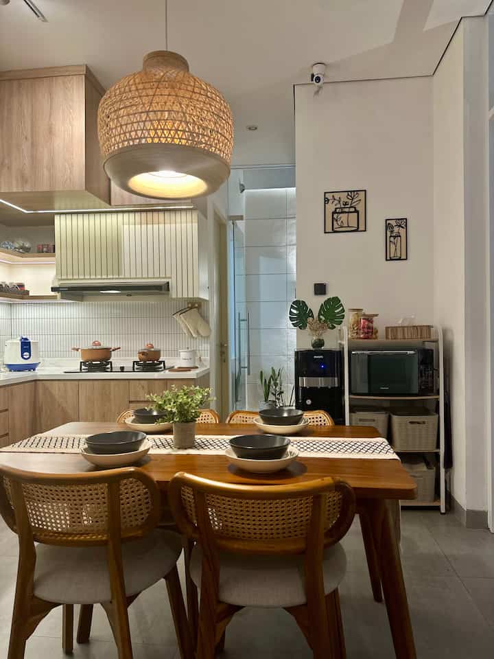 Natural wood tone kitchen dining space featuring wooden dining table and chairs with rattan pendant light in cozy setting