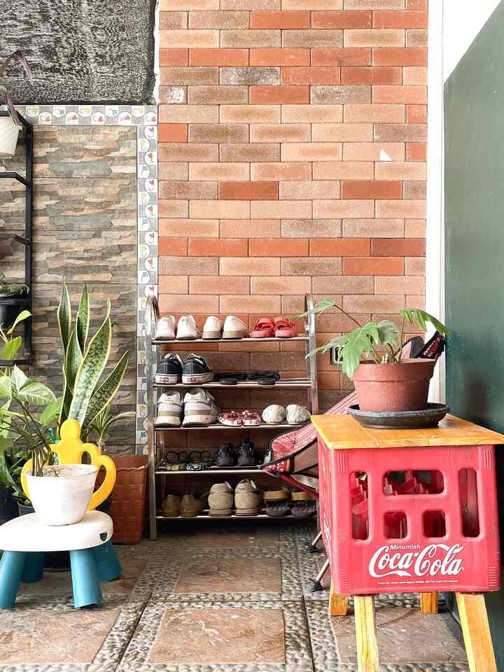 Red brick wall entrance area featuring a stainless steel shoe rack and potted plants creating a natural feel